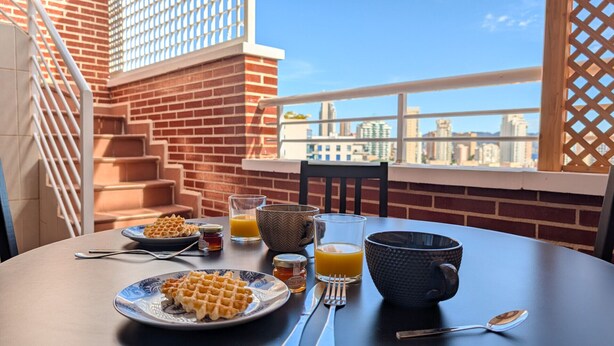 A breakfast setup with waffles, orange juice, and honey on a balcony with a city view. - BULEVAR rooftop apartment (La Vila Joiosa)