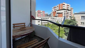 A balcony with a wooden table and chairs, a window with a view of multi-story buildings. - Cozy studio with WiFi and AC in nice Tiranë (Tiranë)