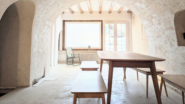 A rustic room with a high ceiling, wooden beams, and a large window. There is a wooden table and benches. - Charming semi-troglodyte house, Amboise (Amboise)