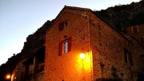 A stone building with a single window and a lit lamp post. - LA TERRASSE DE PEYRE room "La Provençale (Comprégnac)