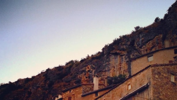 A stone building with multiple levels and an arched entrance, surrounded by a mountainous landscape. - LA TERRASSE DE PEYRE room "La Provençale (Comprégnac)