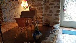 A rustic room with a stone wall, a wooden table, a wicker chair, a large vase with flowers, and a window with a view of the outside. - LA TERRASSE DE PEYRE room "La Provençale (Comprégnac)