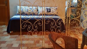 A bedroom with a bed, a wicker chair, and a decorative metal partition. - LA TERRASSE DE PEYRE room "La Provençale (Comprégnac)
