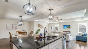 Una cocina moderna con una isla grande, luces colgantes y vistas al salón.