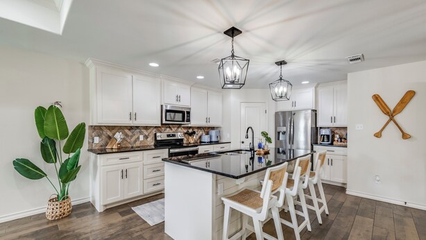 Una cocina moderna con armarios blancos, una isla central con taburetes altos e iluminación colgante.
