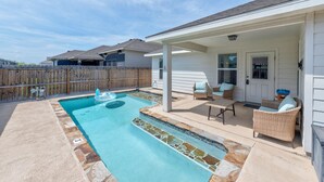 Un patio trasero con piscina, mobiliario exterior y una zona de porche cubierta.