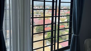 Quarto com uma grande janela que oferece vista para uma área residencial, com casas e uma colina ao longe.