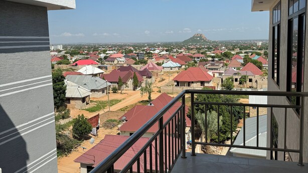 Uma varanda com vista para uma área residencial, com casas de telhados vermelhos e uma montanha ao longe.