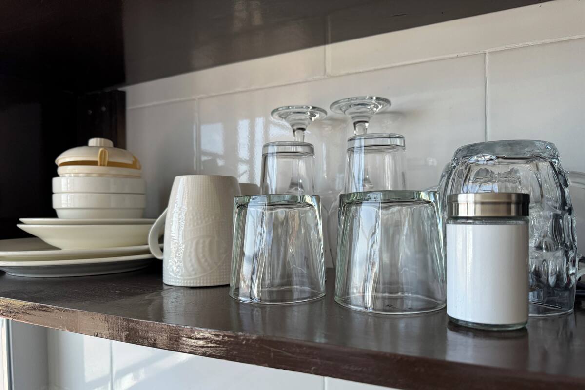 Una encimera de cocina con varios vasos, incluyendo una jarra blanca, una taza blanca y varias botellas de vidrio transparente.
