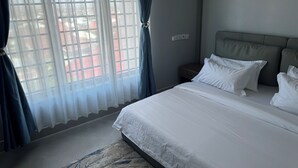 Quarto de hotel com uma cama grande, mesa de cabeceira e janela com cortinas finas.