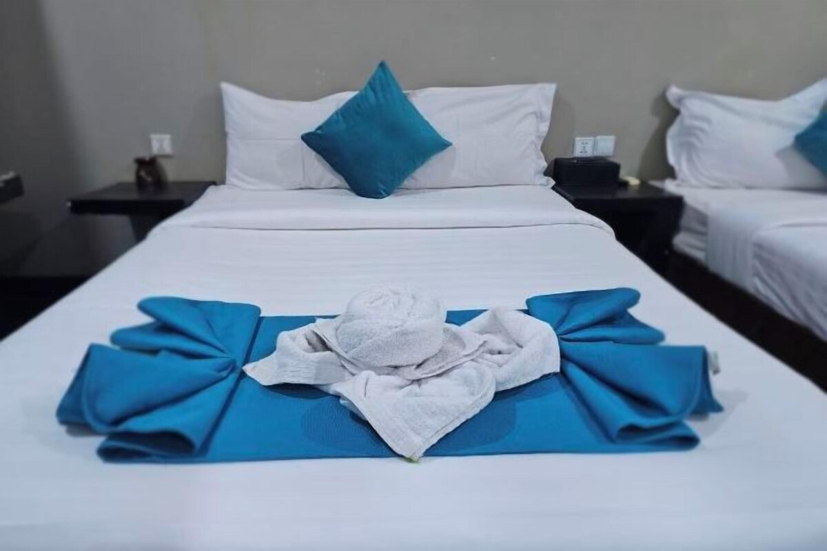 A hotel room with a neatly made bed, a blue towel, and a white bathrobe.