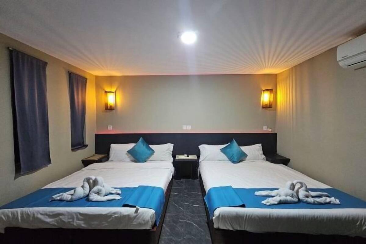 Ett hotellrum med två sängar, var och en med ett blått överkast och vita sängkläder, två väggmonterade lampor och en taklampa.