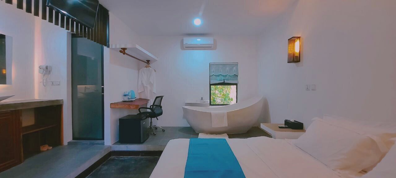 A modern hotel room with a bed, a desk, a chair, a small bathroom, and a large window.
