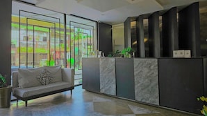 A reception area with a sofa, a reception desk, and a view of the street outside. - Angkor Rise Boutique (Siem Reap)