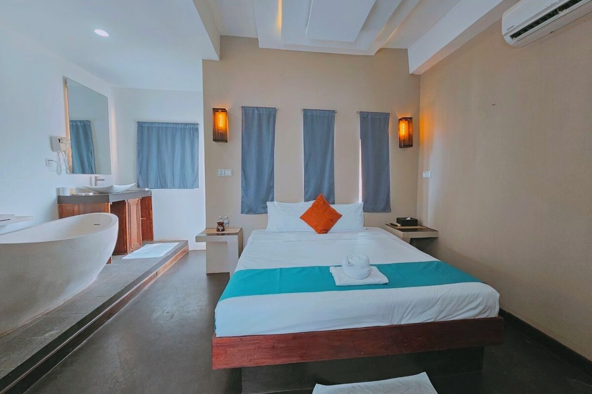 A hotel room with a large bathtub, a bed with a blue accent, and two wall-mounted lights.