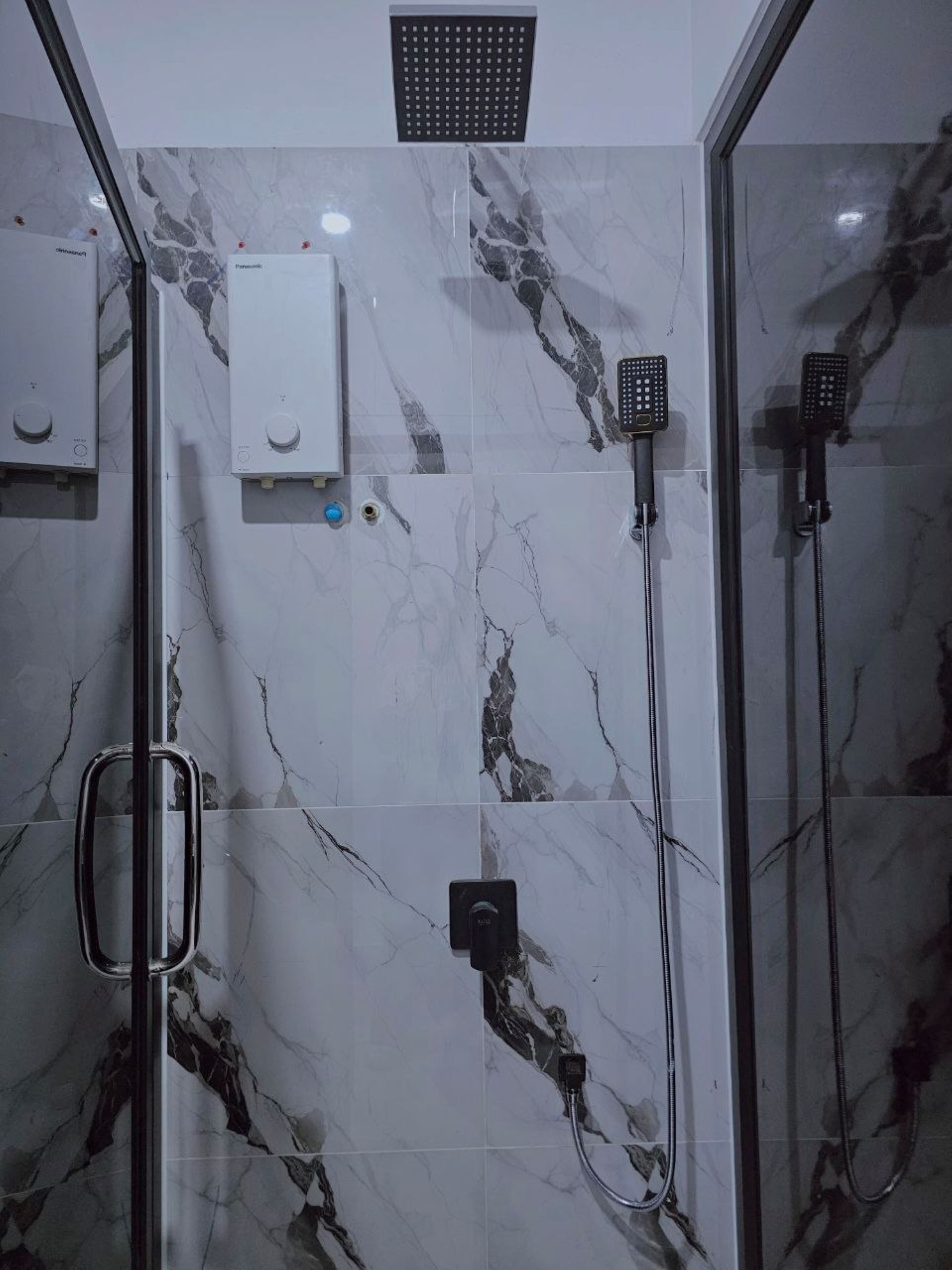 A shower area with a glass enclosure, a handheld showerhead, a wall-mounted showerhead, and a control panel.