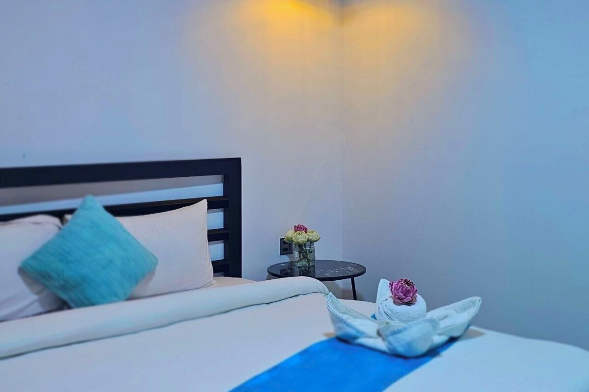 A hotel room with a bed, a bedside table with a vase of flowers, and a lamp.