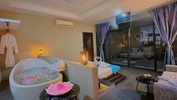 A modern hotel room with a large bathtub, a sofa, a small table, and a balcony with a view.