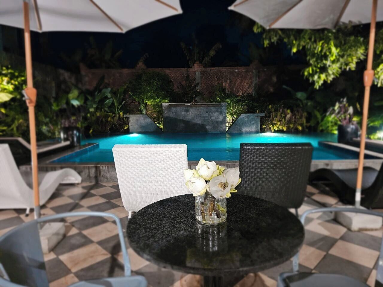 Ein Poolbereich mit Tisch und Stühlen, einer Blumenvase und einem Pool im Hintergrund.
