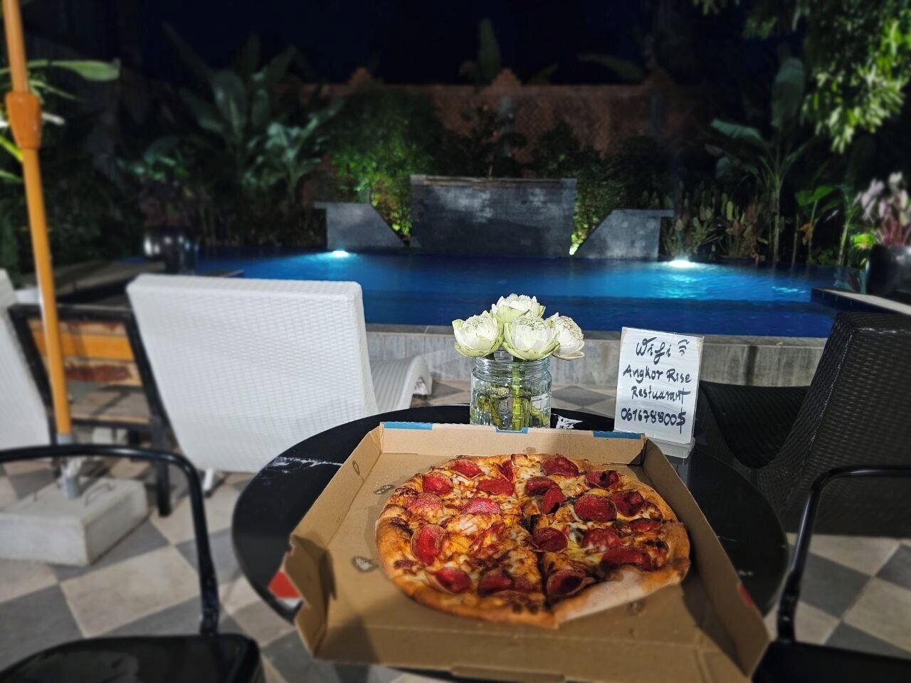 Pizza i en æske, en vase med blomster og et skilt til en restaurant.