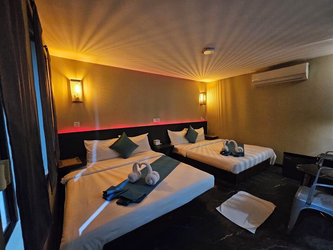 A hotel room with two beds, a desk, and an air conditioning unit.