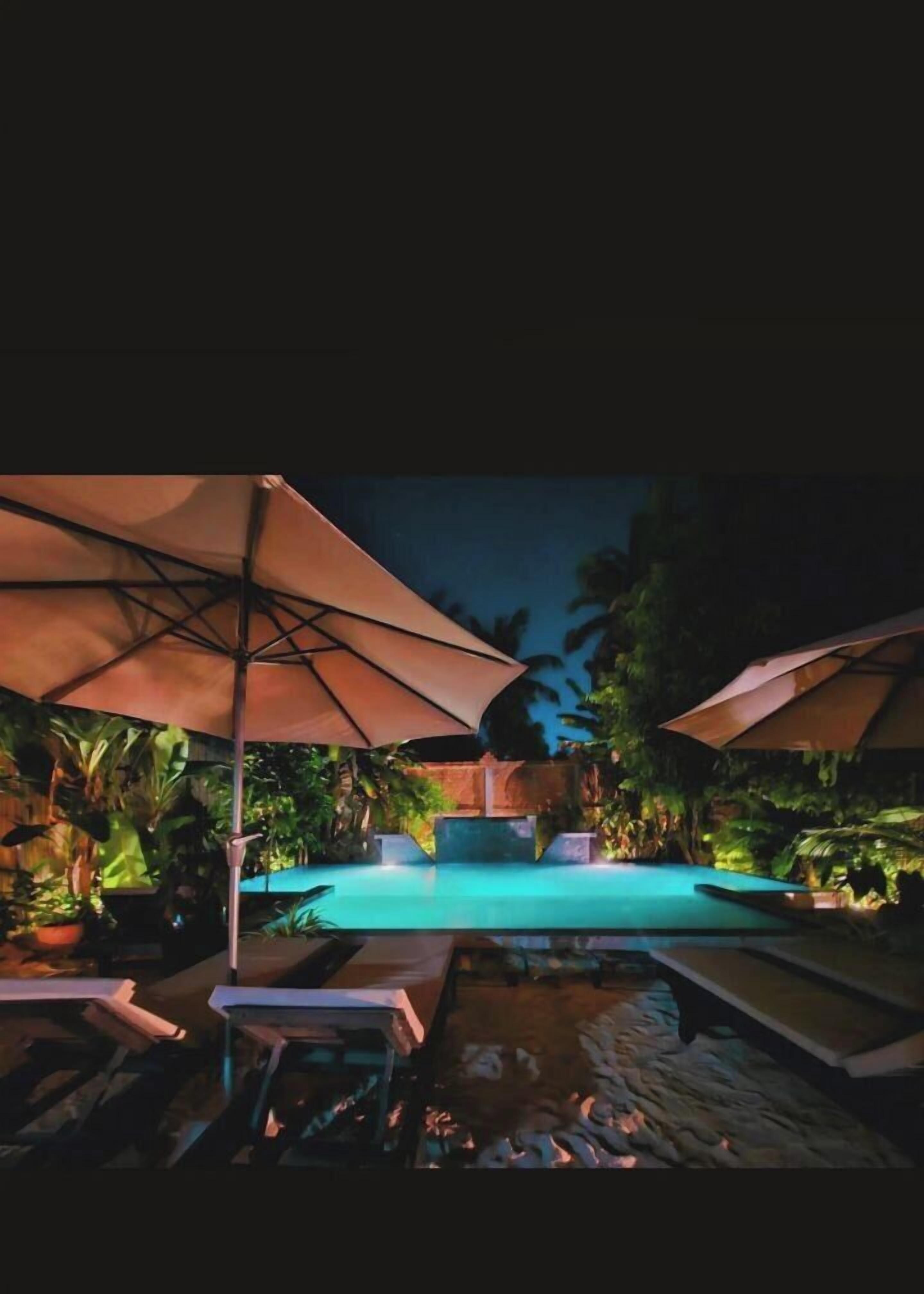 Zona de piscina exterior con sillas de descanso y sombrillas, rodeada de plantas tropicales.
