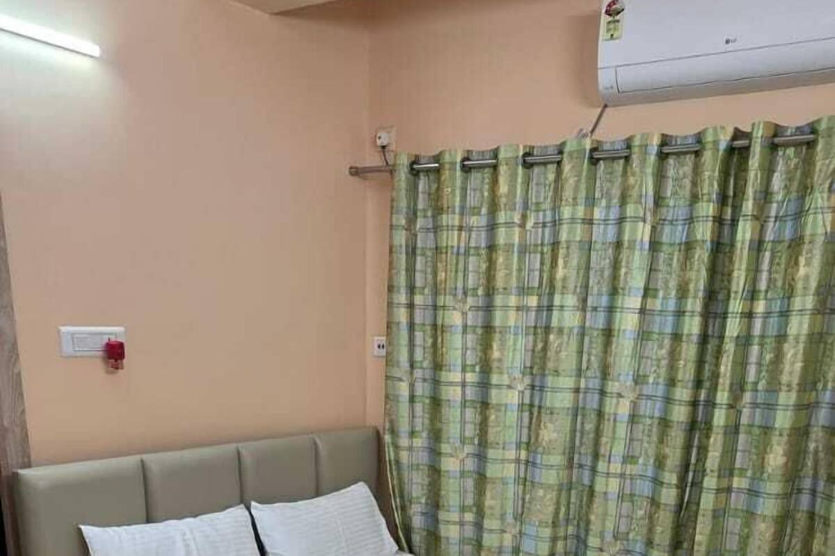A bedroom with a bed, a ceiling fan, a window with curtains, and a wall-mounted air conditioner.