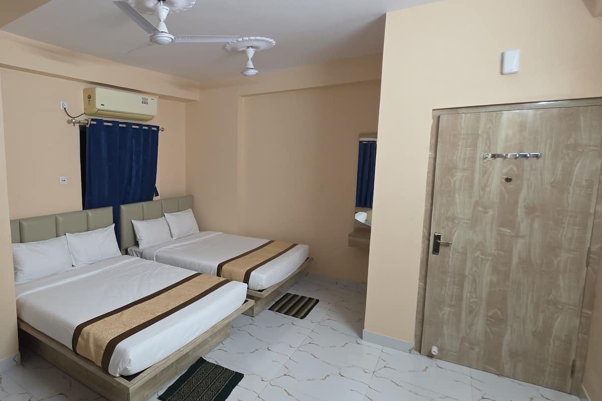 A hotel room with two beds, a wardrobe, a ceiling fan, an air conditioning unit, and a door.