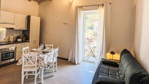 A compact kitchen with wooden beams, a dining table set for four, and a sofa in a bright room with a view through a glass door. - Beautiful private villa for 4 people with A/C, WIFI and terrace (Dolcedo)