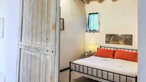 A bedroom with a wooden door, a bed with a metal frame, a nightstand, a lamp, and a window with a curtain. - Beautiful private villa for 4 people with A/C, WIFI and terrace (Dolcedo)