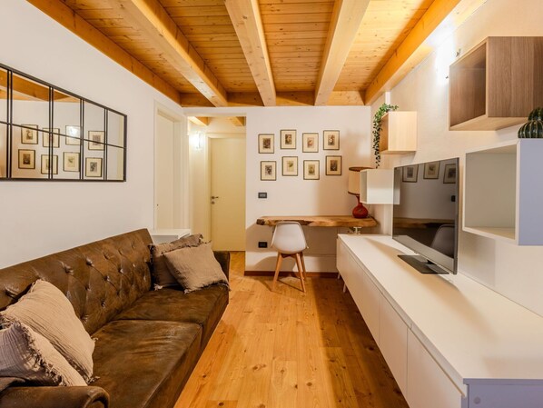 A modern living room with a brown leather sofa, wooden flooring, a white TV stand, and a dining area with a wooden table and chairs.
