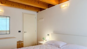 Quarto com cama, mesa de cabeceira, abajur e janela.