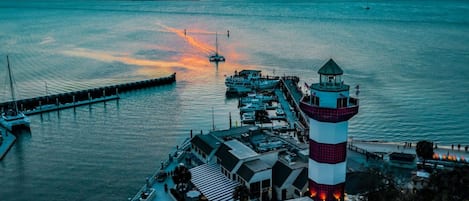 A waterfront property with a lighthouse, docked boats, and a pier extending into the water.