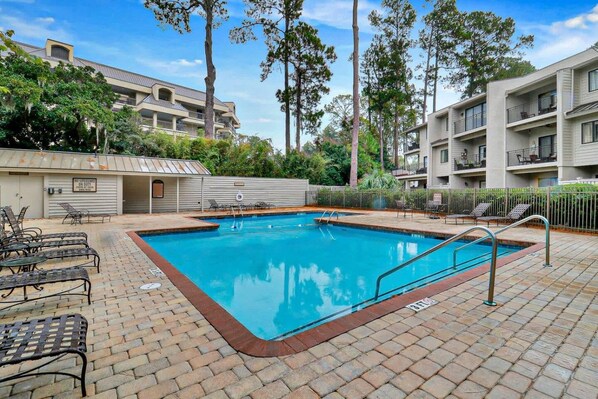 A swimming pool with a lifeguard station, lounge chairs, and a fenced area with trees.