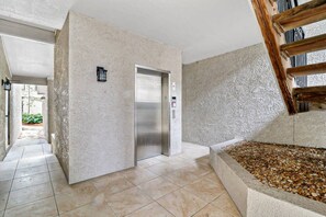 A modern interior with a concrete wall, a metallic elevator, and a stone staircase.