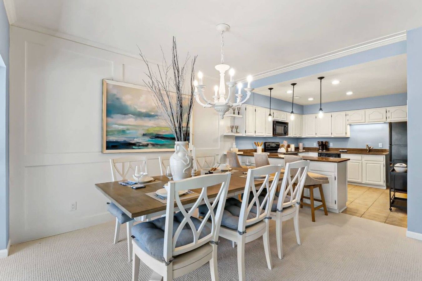 Una cocina moderna con armarios blancos, un comedor con mesa de madera y sillas blancas, y una araña.