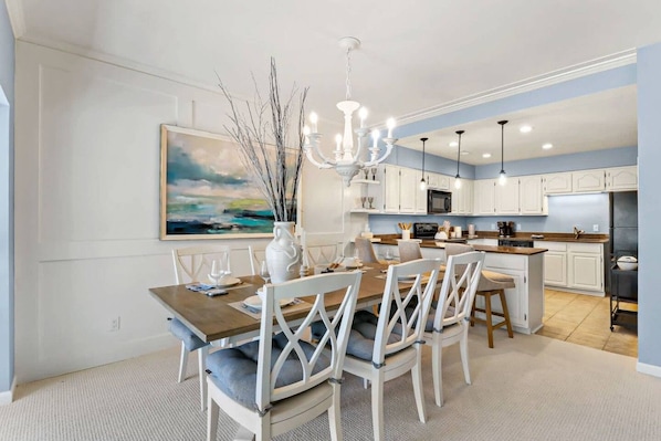 A modern kitchen with white cabinetry, a dining area with a wooden table and white chairs, and a chandelier.