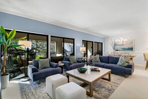 A modern living room with a blue sofa set, a coffee table, and a large window providing a view of the outdoors.