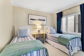 Una habitación con dos camas, una mesita de noche, una lámpara y una ventana con cortinas.