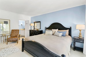 A bedroom with a large bed, a chair, a dresser, and a nightstand.