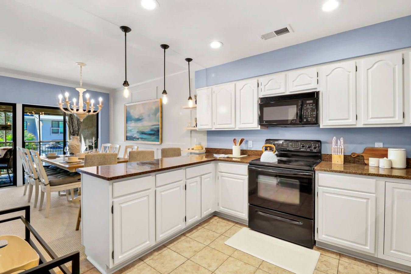 A modern kitchen with white cabinets, a black stove, and a dining area with a table and chairs.