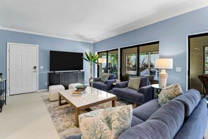 A living room with a sofa, armchairs, a coffee table, a TV, and a plant.