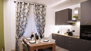 Een moderne keuken met donkere kastjes, een houten eettafel en een raam met gordijnen met een bladmotief.