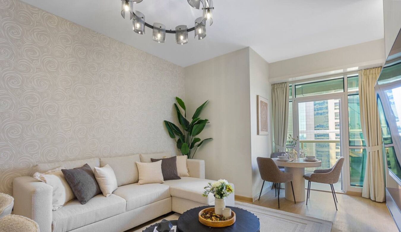 A living room with a sectional sofa, a dining area with a round table, and a large window with curtains.