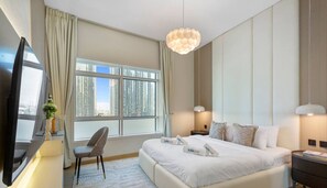 A hotel room with a large bed, a desk with a flat-screen TV, a chair, and a large window offering a city view.