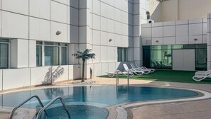 A swimming pool with lounge chairs and a palm tree in a courtyard with a modern building in the background.