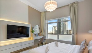 Moderni hotellihuone, jossa on suuri sänky, seinälle asennettu taulutelevisio, työpöytä tuolilla sekä suuri ikkuna, josta avautuu näkymä kaupunkiin.