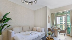 Habitación de hotel con sofá, una mesa de comedor con sillas, una planta en maceta y vistas a la ciudad a través de grandes ventanales.