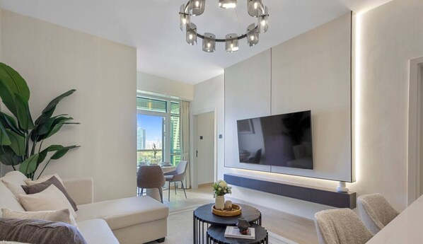 A modern living room with a large flat-screen TV mounted on the wall, a round coffee table with decorative items, and a comfortable seating area with sofas.