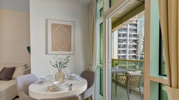 Un comedor con una mesa redonda dispuesta para cuatro personas, un jarrón con flores y una obra de arte enmarcada en la pared.